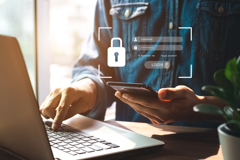 Person using a smartphone and laptop, with a digital login interface and padlock icon shown, symbolising online security.