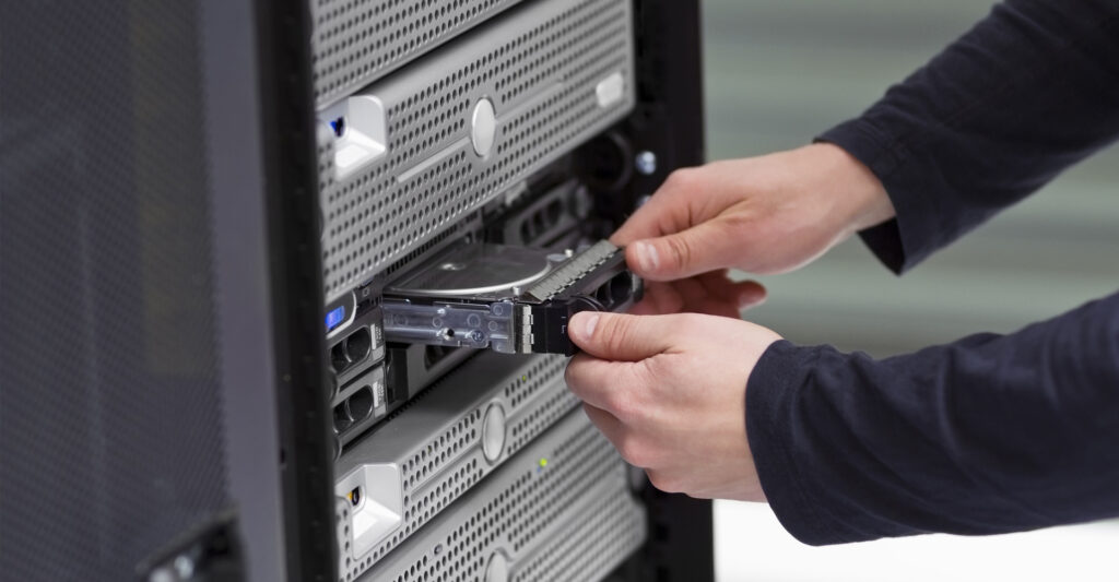 Hands inserting or removing a hard drive from a server rack in a data centre environment.