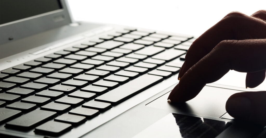 A hand using the trackpad of a laptop, with the keyboard in the background.