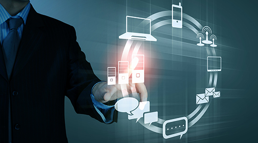 A person in a suit touches virtual icons of technology devices, cloud storage, and communication symbols on a digital screen.