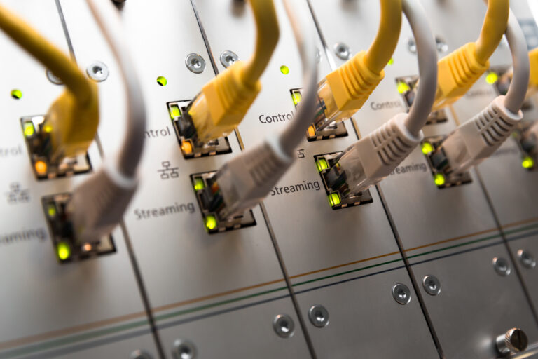 Close-up of several Ethernet cables plugged into a network switch, with green indicator lights illuminated next to each port.