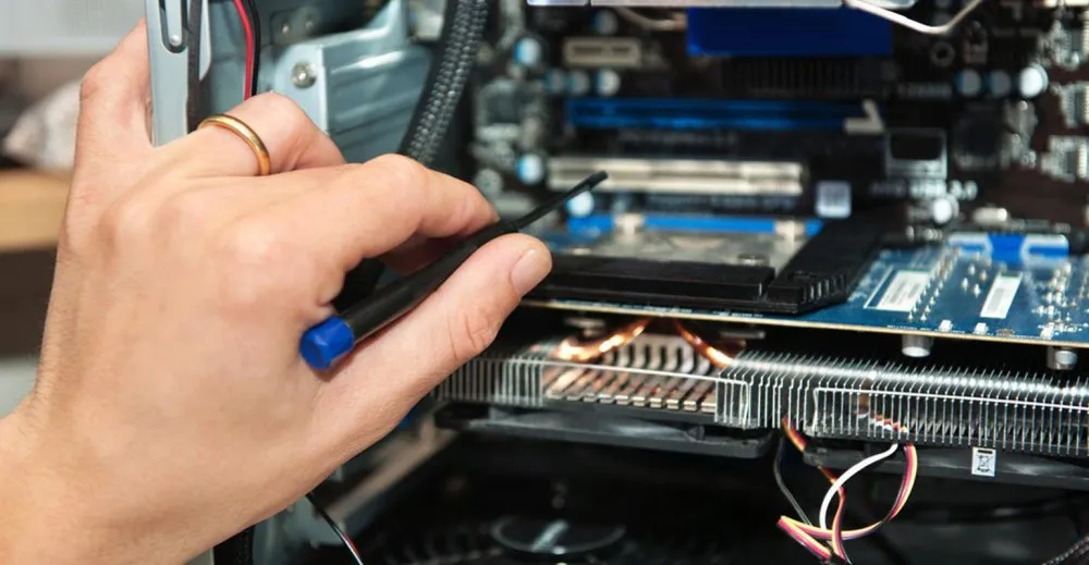 A hand holding a screwdriver works inside an open computer case, adjusting components on the mainboard.