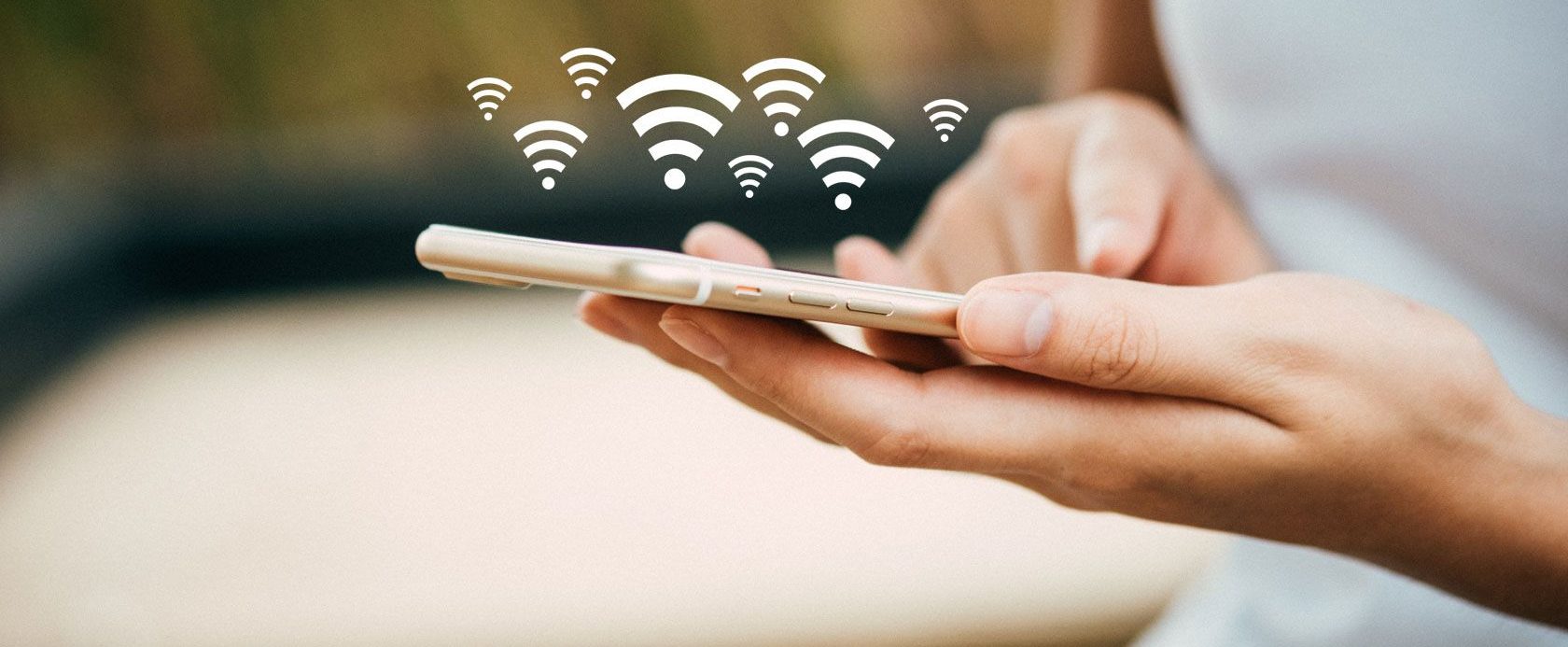 A person holding a mobile phone with Wi-Fi symbols illustrated above the device, suggesting wireless connectivity.